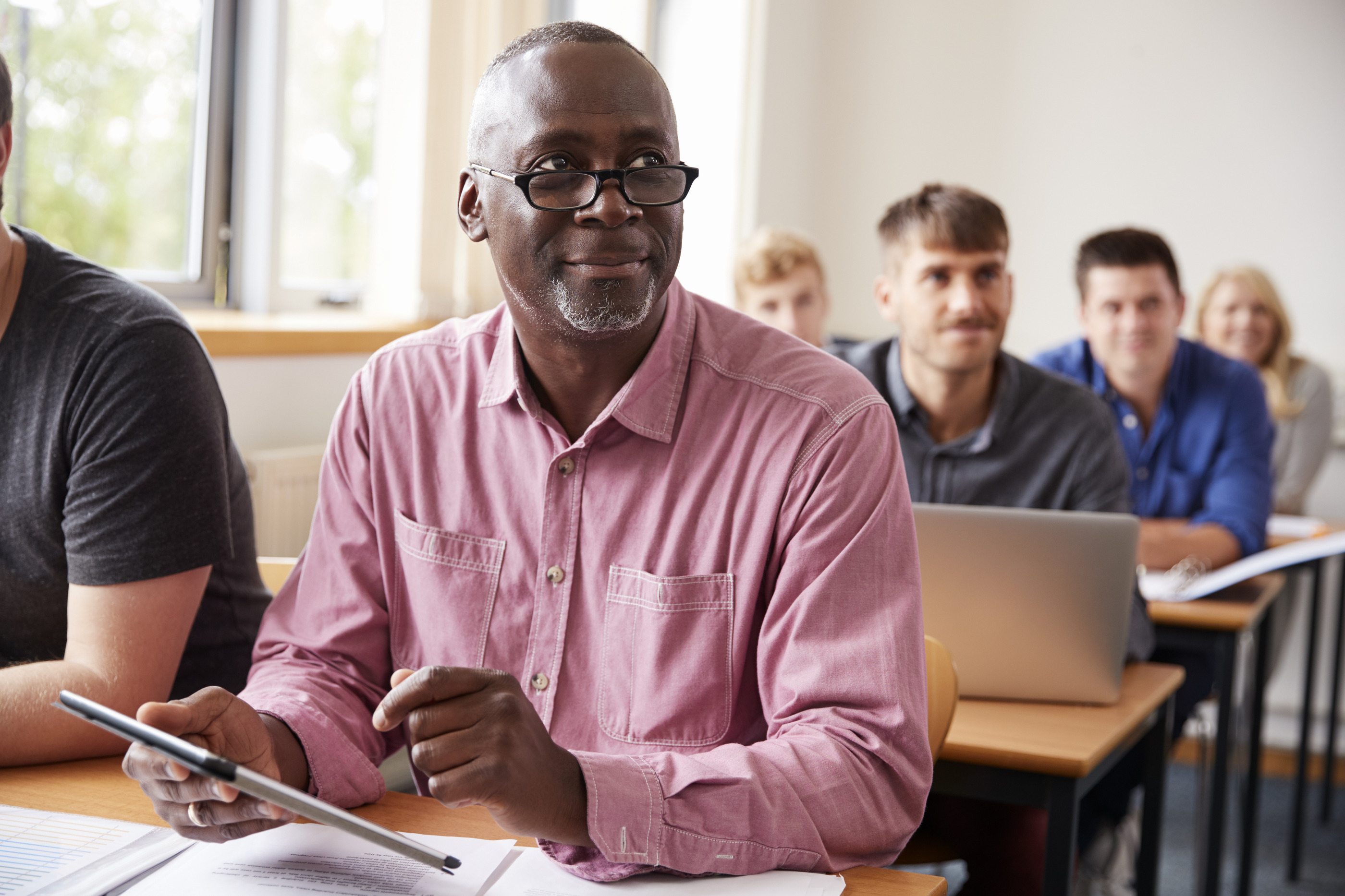 An older learner in a classroom holding a tablet during a session